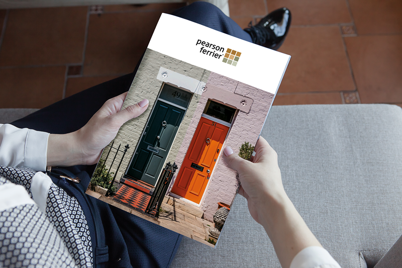 This image shows a Pearson Ferrier brochure being held by a woman. You can't see the woman's body or face it is from the angle of her eyes looking downwards.